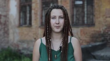 Rasta saçlı güzel bir genç kız eski harap olmuş bir binanın arka planında kamera karşısında bir rapor tutuyor. Yakın plan.