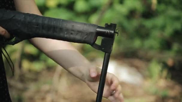 Close-up van de hand van een jong meisje met afro-vlechten die een geweer oplaadt en schiet in het bos — Stockvideo
