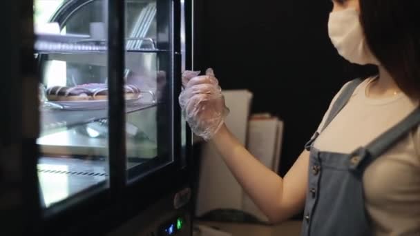 Joven barista en máscara médica y guantes protectores en el trabajo en una cafetería durante la pandemia de coronavirus. Primer plano . — Vídeo de stock