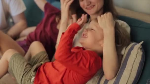 幸せな若い家族は一緒にソファで遊び、若い子供たちと笑って家に座って時間を過ごします。閉鎖 — ストック動画
