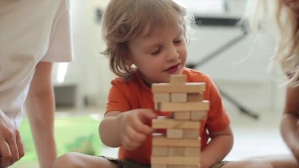 Los niños juegan el rompecabezas y el niño se ríe de toda la construcción de los bloques de madera que se derrumba. Primer plano — Vídeos de Stock