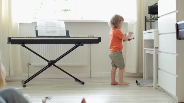 Lustig liten pojke lägger en leksaksbuss på en hylla i ett rum där fönstret står en synt och springer iväg. Närbild — Stockvideo