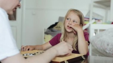 Ciddi küçük bir kız babasıyla bir masa başında konuşuyor. Git ve sonra küçük kardeşine kapıyı açmak için ayağa kalkıyor. Kamera odağı değiştiriyor. Yakın plan.