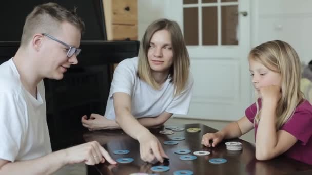 Menina de cabelos compridos joga entusiasticamente um jogo de tabuleiro Memo com adultos sentados em uma mesa na sala. Close-up — Vídeo de Stock