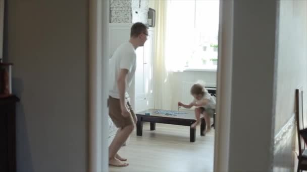 Un padre e suo figlio in identiche t-shirt bianche e pantaloncini kaki si allenano insieme nella stanza e saltano in alto insieme. Primo piano — Video Stock