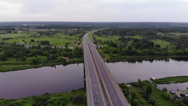 Pomalá střelba z helikoptéry širokého silničního mostu přes řeku a panorama zelených luk a lesů s výhledem na obzor — Stock video