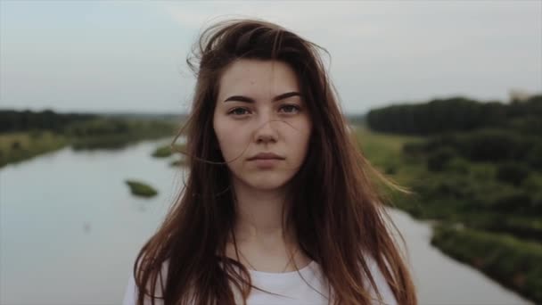 Retrato de una hermosa chica sensual que se encuentra en el puente en un día de verano contra el telón de fondo del río y el bosque y sonríe muy bien. En cámara lenta. . — Vídeo de stock