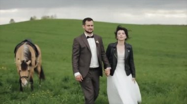 Yeni evliler kırsalda otlayan bir atın yanında yürürken el ele tutuşuyorlar. Yakın plan. Yavaş çekim. Kamera yukarıdan aşağıya hareket eder