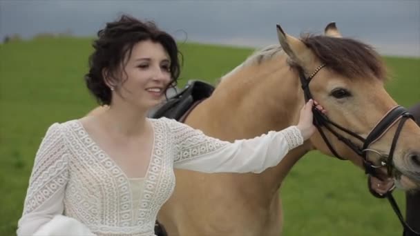 The bride and groom hold a horse on both sides and walk along a green meadow. View from the side. Close-up. Slow-motion — Stock Video