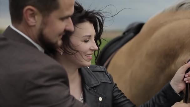 Os recém-casados estão em um pasto de fazenda com um cavalo e em conjunto mantêm-no abaixo de um freio. Vista de lado. Close-up. Movimento lento — Vídeo de Stock