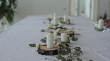 Düğün masasının şenlikli tasarımı. Bir kadın çiçeklerin arasına ahşap dairelere mum konmuş cam vazolar yerleştiriyor. Yakın plan.