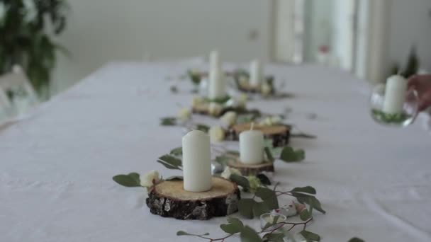 Праздничный дизайн свадебного стола. Женщина ставит стеклянные вазы со свечами на деревянных кругах среди цветов. Крупный план — стоковое видео