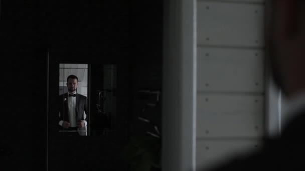Spiegelung im Spiegel eines jungen bärtigen Mannes, der seinen schwarzen Anzug anpasst. Ein junger Bräutigam in weißem Hemd und Fliege. Nahaufnahme — Stockvideo