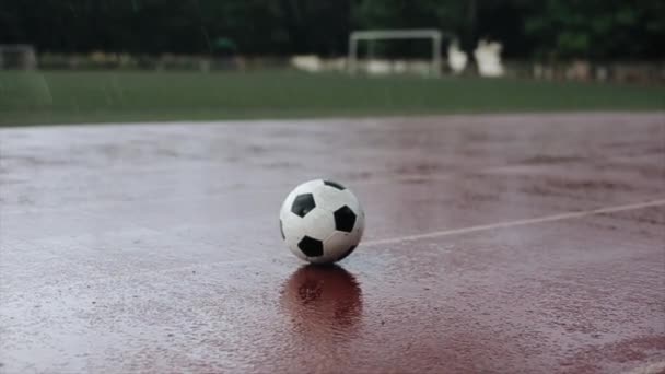 Närbild av fotboll som ligger på stadion löpband i kraftigt regn mot bakgrund av ett fotbollsmål. Kameran ändrar fokus — Stockvideo