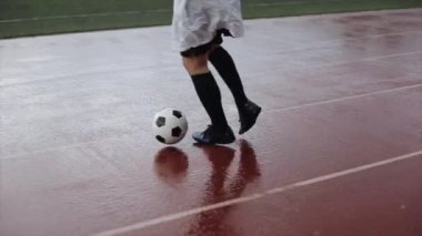 Antrenmandaki bir futbol kulübünün atleti bardaktan boşanırcasına yağmur yağarken stadyumun koşu bandına top dolduruyor. Yakın plan.