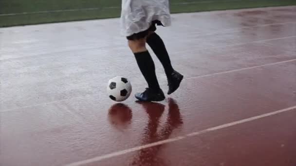 Un atleta de un club de fútbol en el entrenamiento suministra una pelota en la cinta de correr del estadio bajo la lluvia. Primer plano — Vídeos de Stock