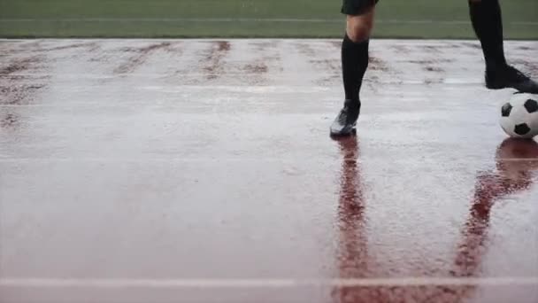 Fotbalový hráč v tréninku pláštěnky a kopne do míče v dešti. Kamera se pohybuje zdola nahoru. Detailní záběr — Stock video