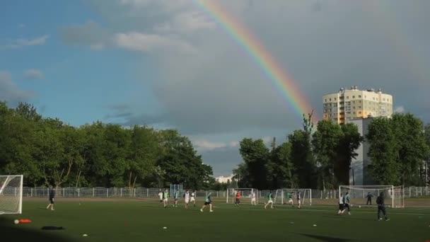 Minsk, Biélorussie - 23 juin 2020 : L'équipe de football s'entraîne et joue au football dans un stade ouvert sur fond d'arc-en-ciel lumineux dans le ciel nuageux — Video