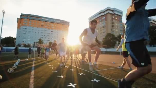 Hráči fotbalového klubu trénink provádět skákání přes překážky na městském sportovišti proti zapadajícímu slunci. Detailní záběr. Model obnoven — Stock video