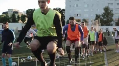 Günlük futbol kulübü eğitimi. Futbol sahasındaki oyuncular engellerin ve futbol toplarının üzerinden atlıyorlar. Yakın plan. Model Gerçekleştirildi