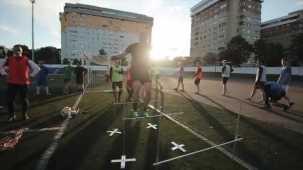 L'équipe de football s'entraîne sur le terrain de football. Les joueurs sautent par-dessus les barrières et les balles de football dans les rayons du soleil couchant. Gros plan. Modèle Réalisé — Video