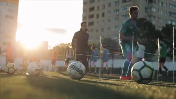 Výcvikový proces fotbalového týmu. Hráči skok přes bariéry na pozadí fotbalových míčků ležících v popředí. Detailní záběr — Stock video