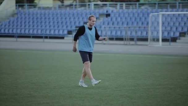 Στην προπόνηση της ποδοσφαιρικής ομάδας. Ο παίκτης περπατά στο γήπεδο ποδοσφαίρου με ένα αστείο βάδισμα στο παρασκήνιο των θέσεων για τους θεατές. Κοντινό πλάνο — Αρχείο Βίντεο