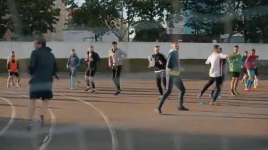 Futbolcular ısınıyor. Spor sahasında koşma egzersizleri. Geçit ızgarasından ateş ediyorlar. Arka planda bulanıklık. Yakın plan. Model Gerçekleştirildi