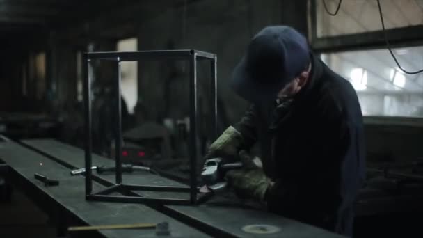 Un fabbro in un'officina lavora saldature su un prodotto metallico utilizzando uno strumento di rettifica elettrico. Le scintille volano dalla macinazione. Vista laterale — Video Stock