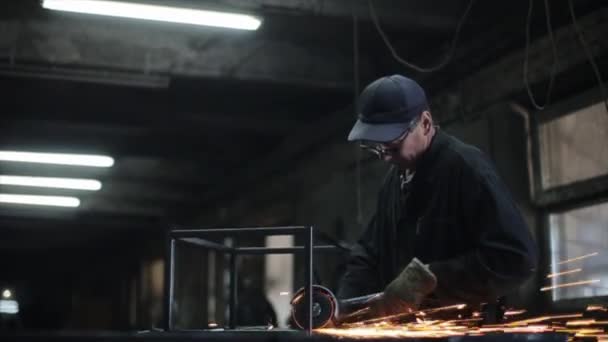 Un cerrajero en un taller procesa soldaduras en un producto metálico usando una herramienta de molienda eléctrica. Las chispas vuelan de la molienda. Vista lateral — Vídeo de stock