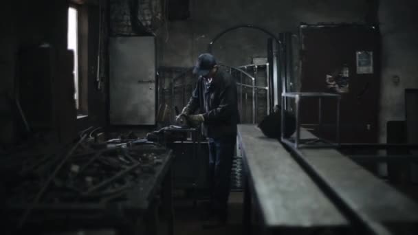 Работник в бойлерном костюме в мастерской полирует сварные швы на металлической конструкции. Искры от шлифовального электроинструмента — стоковое видео