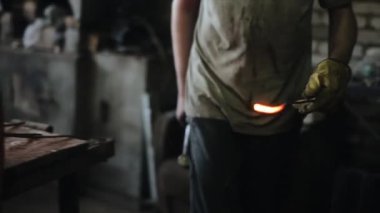 Demirci, demircilerin ocak manzarasının yanında duran örsün üzerinde kızgın demir bir çubuğa vurur. Yakın plan.