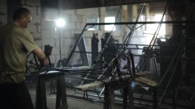 Bir atölye çalışanı, üzümlerin ve yaprakların dövüldüğü metal bir ürüne elektrik spreyinden siyah boya püskürtür.