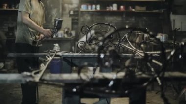 Usta, atölyedeki elektrikli spreyden dövülen metal bir sanat eserini resmediyor. Kamera kaymaları güzel ürün detaylarına odaklanır