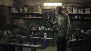 Atölyede kirli bir tişört giyen yetişkin bir adam güzel bir sanat eserini sprey boyayla boyuyor. Yan görünüm