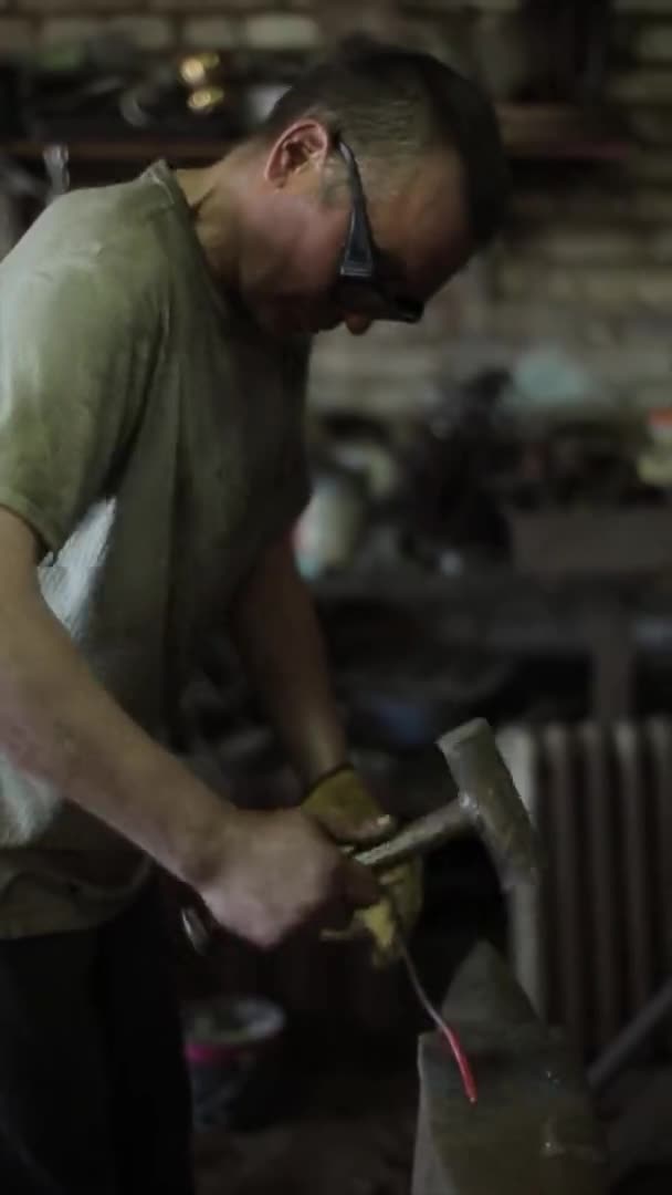 Vídeo vertical. Um homem bate na vara de ferro quente vermelho um martelo em um forno de ferreiros com um martelo em uma bigorna. Close-up . — Vídeo de Stock