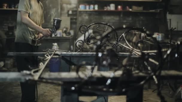 Der Meister bemalt in der Werkstatt ein Kunstwerk aus Metall, das aus einem elektrischen Sprayer geschmiedet wird. Kamera verlagert Fokus auf schöne Produktdetails — Stockvideo