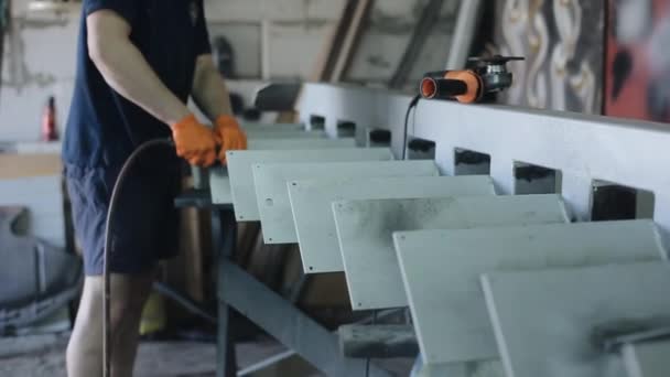 Um trabalhador em uma camiseta azul e shorts em luvas de proteção laranja faz furos em uma estrutura de metal branco com ferramentas elétricas. Close-up — Vídeo de Stock
