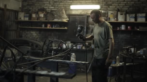 En vuxen man i smutsig t-shirt i verkstaden målar en vacker konstsmidd produkt med sprayfärg. Sidovy — Stockvideo