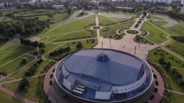 Şehrin yeşil bölgesindeki ve şehrin panoramasının karşısındaki yuvarlak buz arenasının havadan görünüşü. Yavaş çekim.