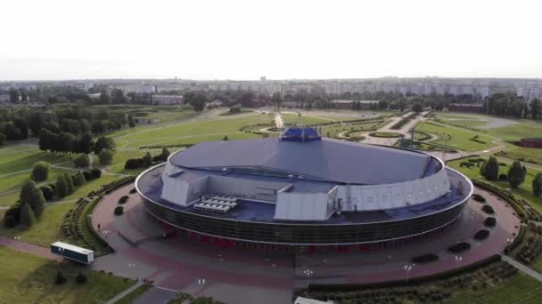 Shooting from the copter of the round ice arena against the backdrop of the cityscape among the green lawns. The camera is moving from the bottom up — Stock Video