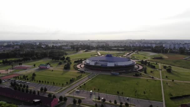 Uma vista aérea da arena de gelo de hóquei redondo localizado área entre os gramados e árvores contra o pano de fundo da paisagem urbana — Vídeo de Stock