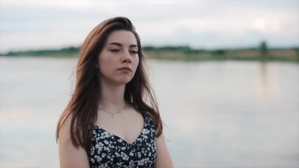 Retrato de una joven tranquila que se para con los ojos cerrados en la orilla del río y medita. Movimiento lento — Vídeos de Stock