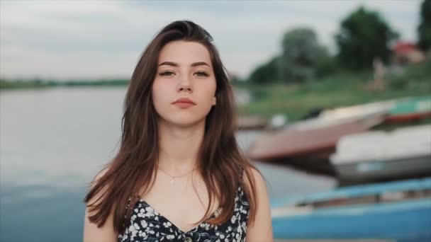 Nazik genç bir kız bir yaz günü nehir kenarında durur ve saçını düzleştiren kameraya bakar. Yakın plan. Yavaş çekim — Stok video