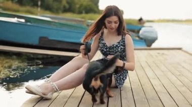 Uzun saçlı tatlı kız esmer köpek dachshund cinsi köpeğiyle bir yaz günü nehrin kıyısındaki ahşap iskelede oynuyor. Yakın plan.