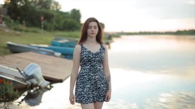 Romantik genç kız bir yaz günü gün batımında nehir kıyısında yürüyor. Yakın plan. Ağır çekim. Bulanık arkaplan