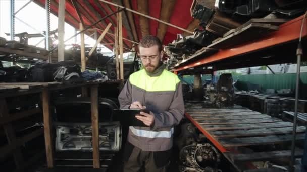 Un service responsable de voiture de jeune ouvrier dans un uniforme gris garde une trace des pièces de rechange dans l'entrepôt. Gros plan — Video