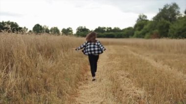Enerjik genç bir kız kollarını açmış buğday tarlasında koşuyor. Köyde dinlen. Yaşam tarzı. Yavaş çekim