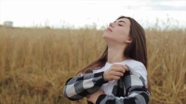 Doğada yürü. Genç bir kız buğday tarlasında duruyor ve gözleri kapalı meditasyon yapıyor. Yakın plan. Yavaş çekim