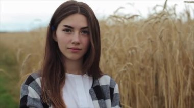 Buğday tarlasında duran gülümseyen genç bir kızın portresi. Yakın plan. Kamera yakınlaşıyor ve uzaklaşıyor.